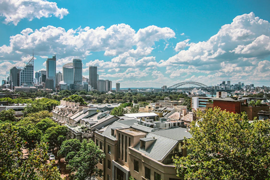 Blue skies and white clouds over residential Sydney with the CBD skyline in the background.