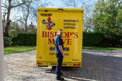 Bishop's Move employee standing by the back doors of a yellow removals van.