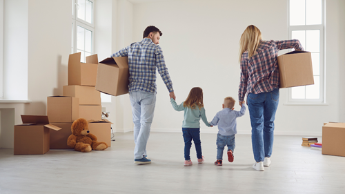 Young family moving house and carrying boxes while holding hands