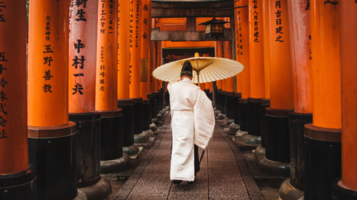 Man in traditional Japanese clothing holding an umbrella and walking alongside orange columns