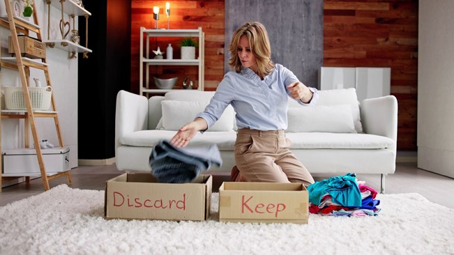 A woman decluttering her clothes by sorting them into boxes labelled ‘Keep’ and ‘Discard.’