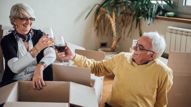 An elderly couple toasting a glass of wine to each other after moving into their new home.