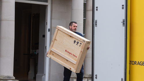 Bishop’s Move team member carrying a wooden crate towards a yellow removal van