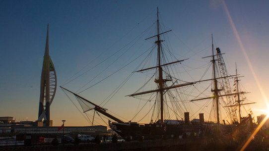 Spinnaker Tower as a backdrop for a moored naval ship in Portsmouth at sunset.