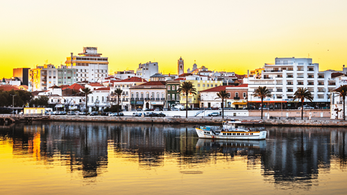 Sunset over Portimão’s white buildings with a fishing boat sailing through