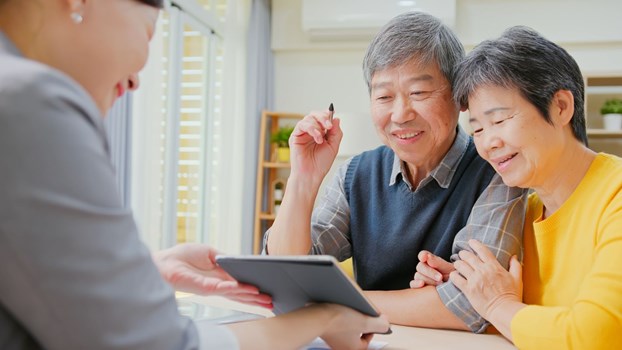 An elderly Asian couple looking at a property on a tablet shown by a female realtor.
