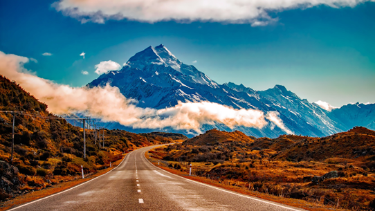A road through burnt orange vegetation towards a snow-capped mountain in New Zealand.