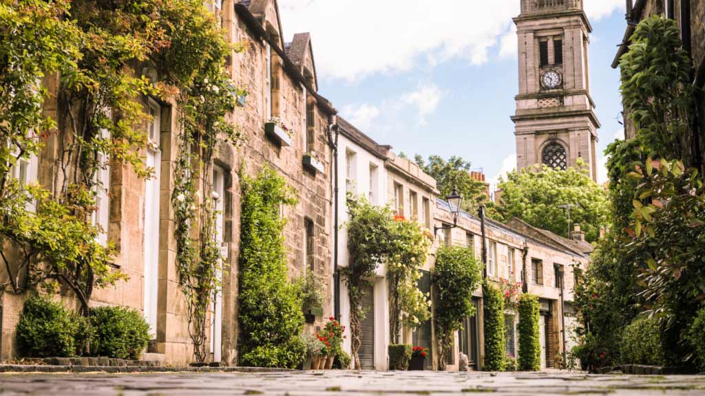 Elegant Victorian homes in Stockbridge with green trees and plants along the street.